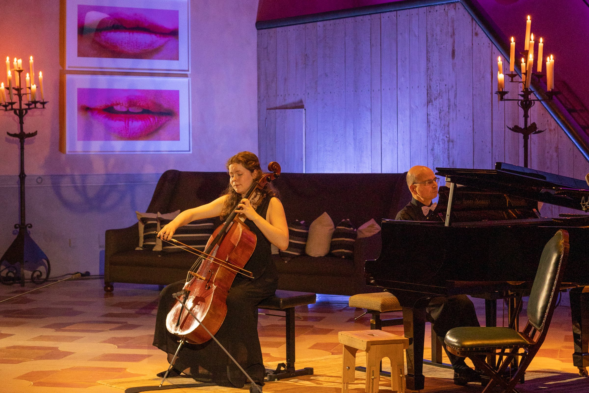 A cellist and a pianist performing in the Classeek showroom, the walls washed in violet and magenta light, amber light on the floor.
